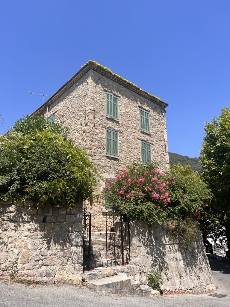 Stone house with green shutters and a gate.